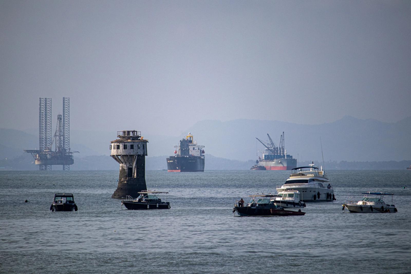 A scenic view of various ships and a tower in Mumbai harbor, India, with an oil rig in the background