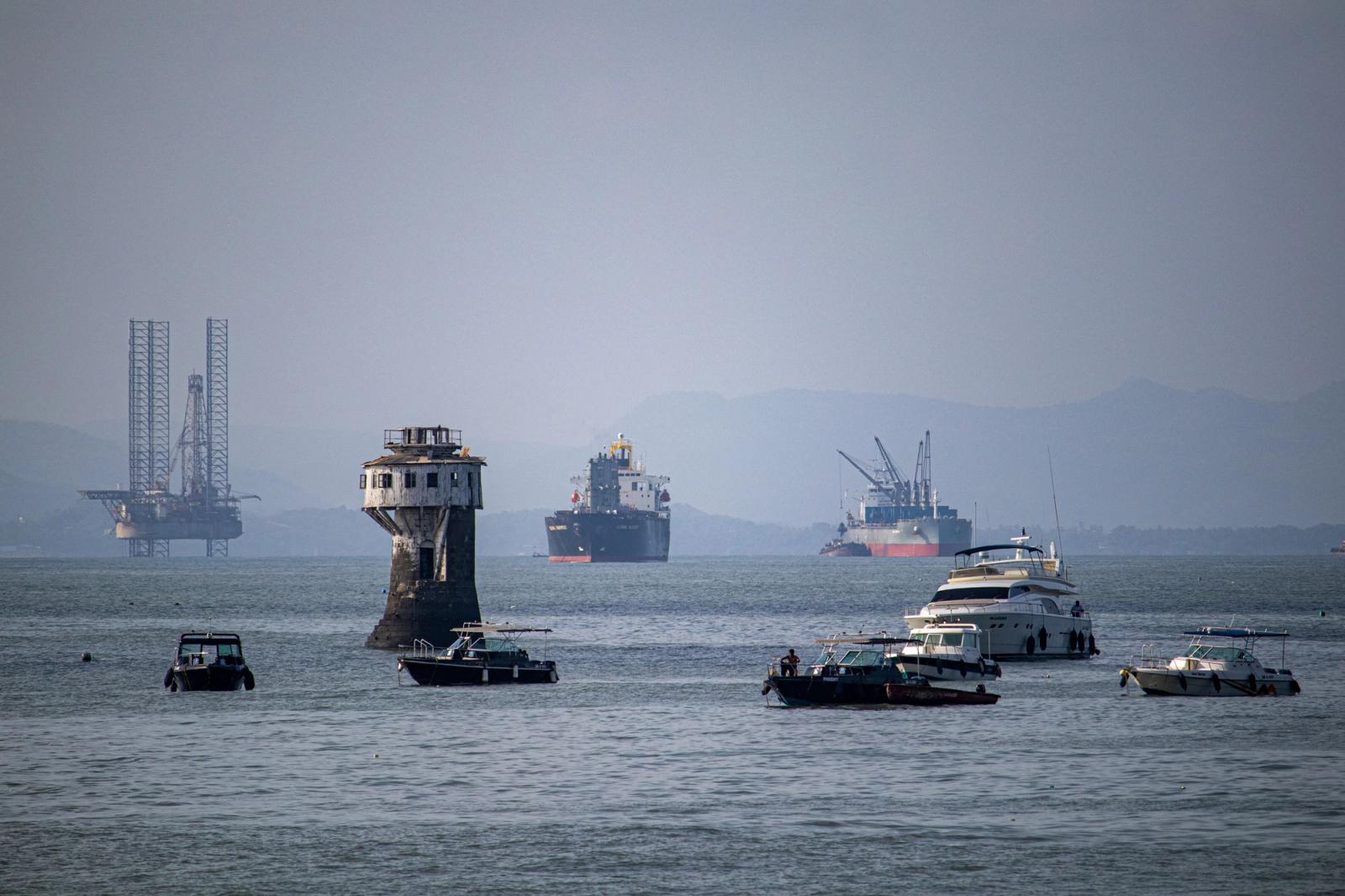A scenic view of various ships and a tower in Mumbai harbor, India, with an oil rig in the background