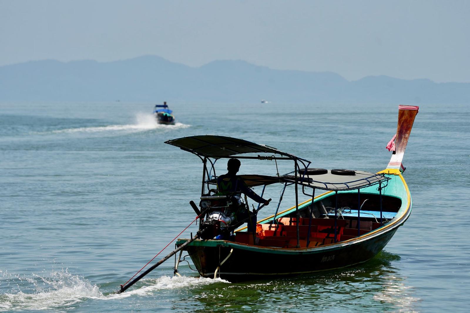 Longtail boat with a captain at the helm cruising a calm bay