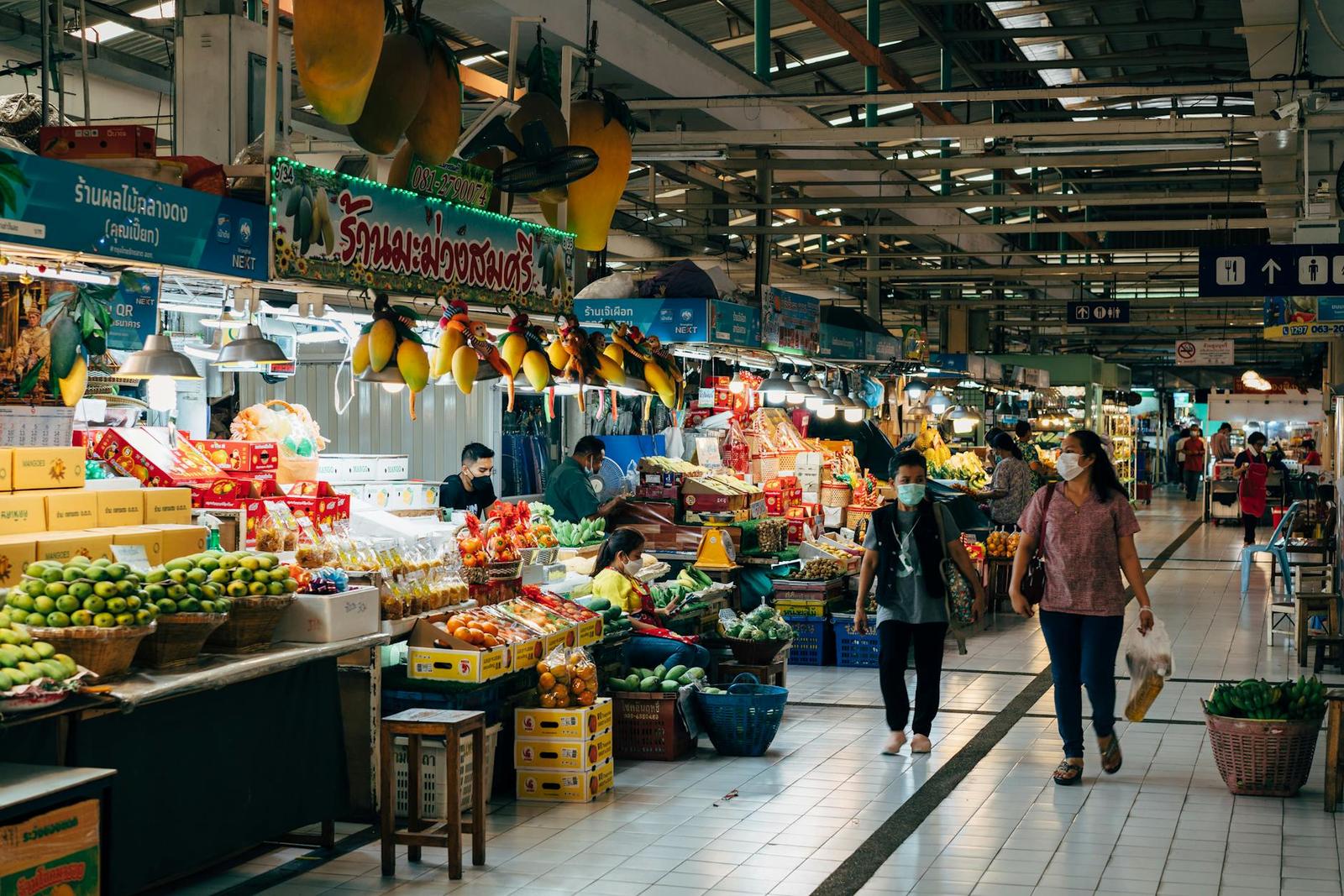 Covered market aisle lined with fresh produce stalls and masked shoppers
