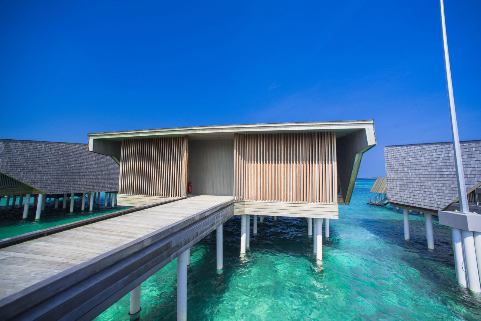 A modern wooden overwater villa on stilts above clear shallow water
