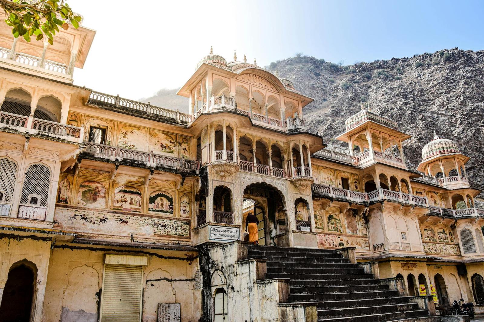 Ornate pink sandstone palace facade with carved balconies against a rocky hillside