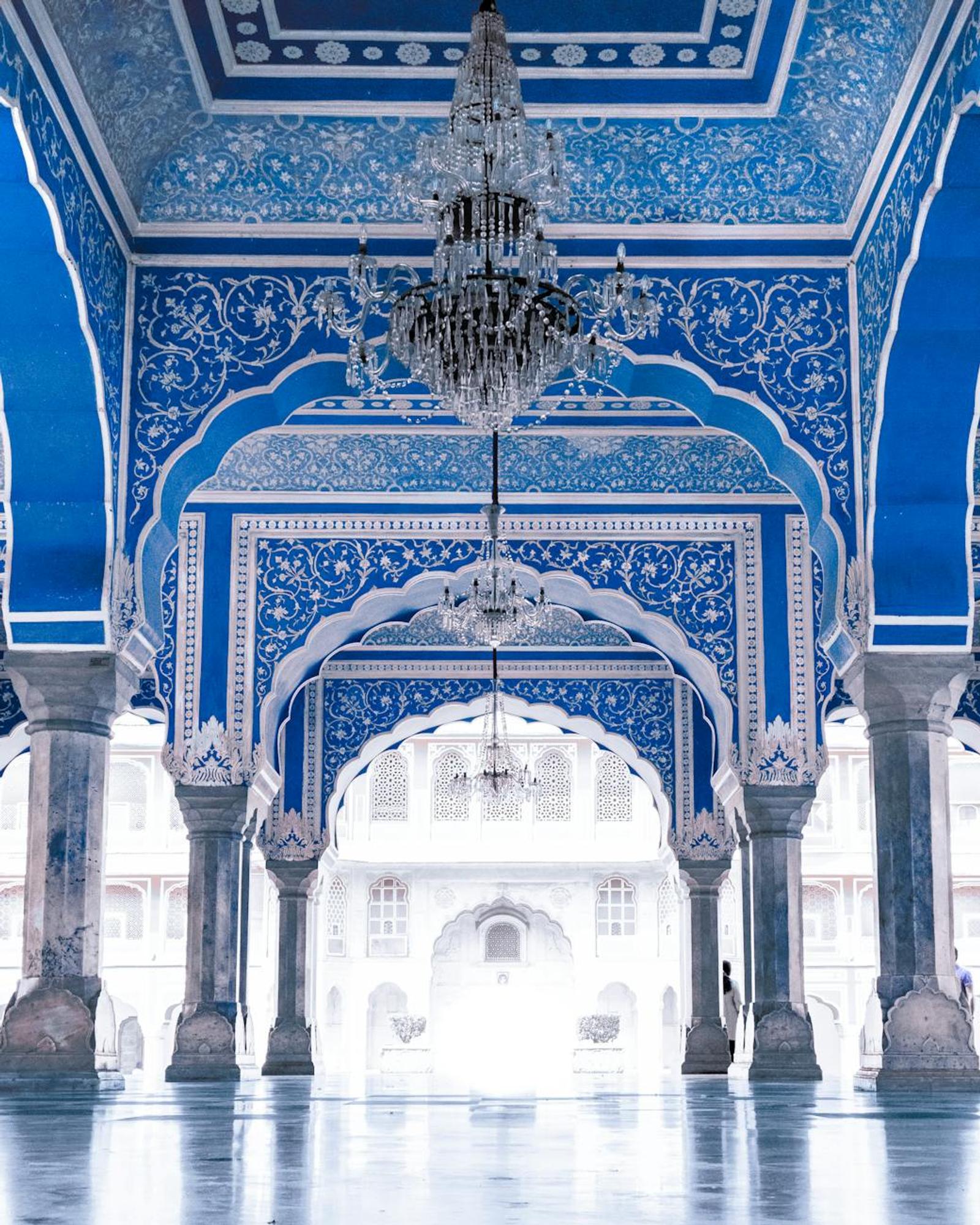 Ornate blue and white mirrored hall with a crystal chandelier and arched doorways