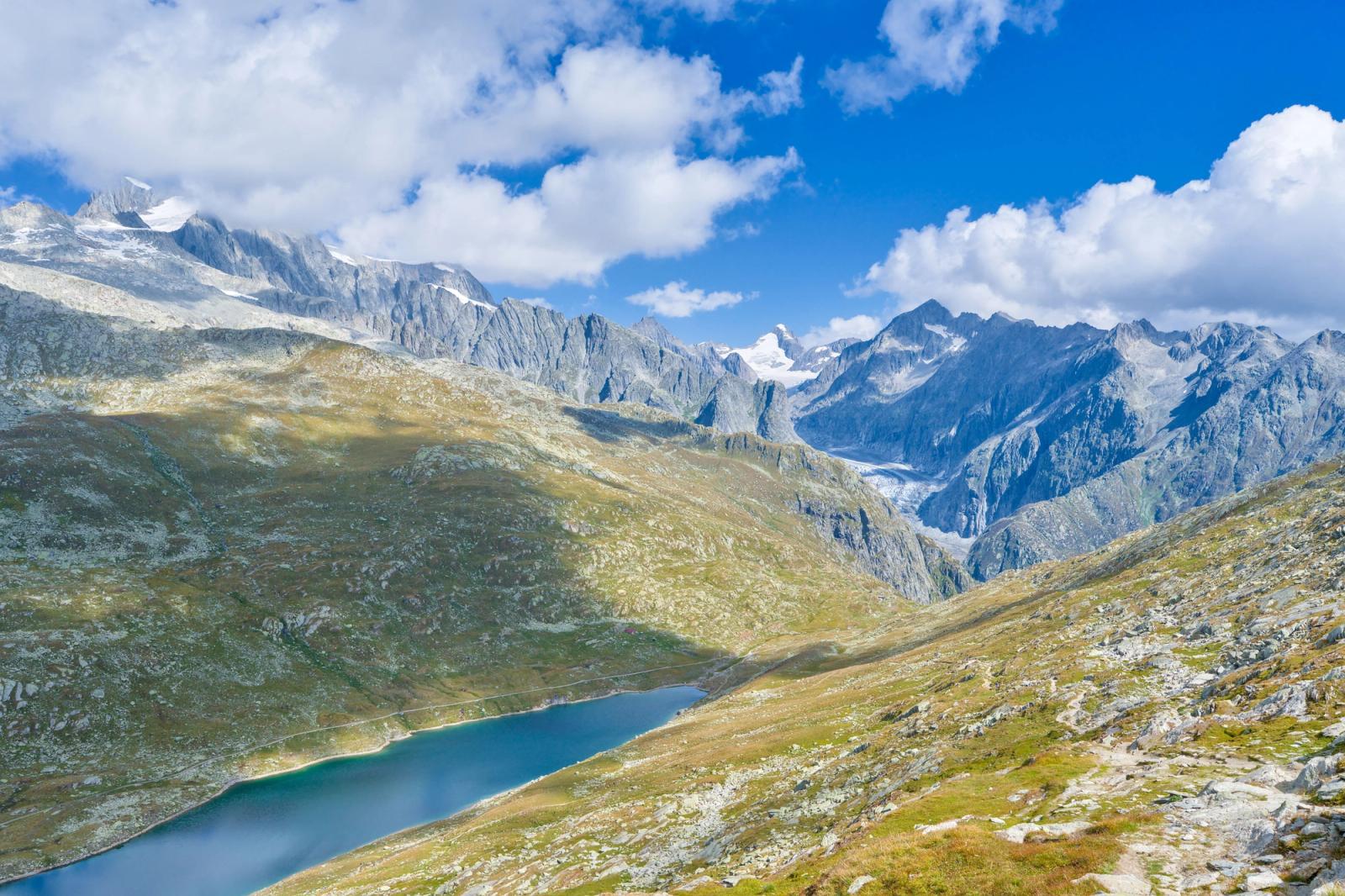 A turquoise glacial lake set in a green alpine valley beneath jagged peaks