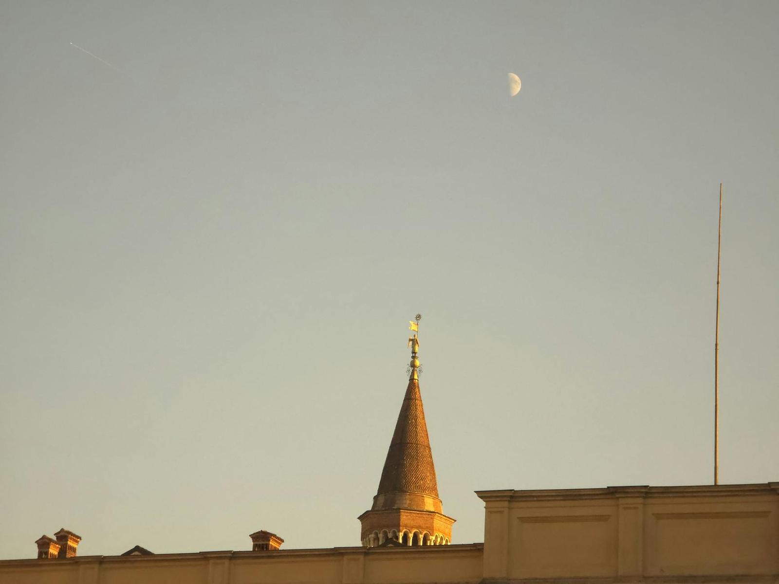 A copper spire catching the light beside a rising half moon