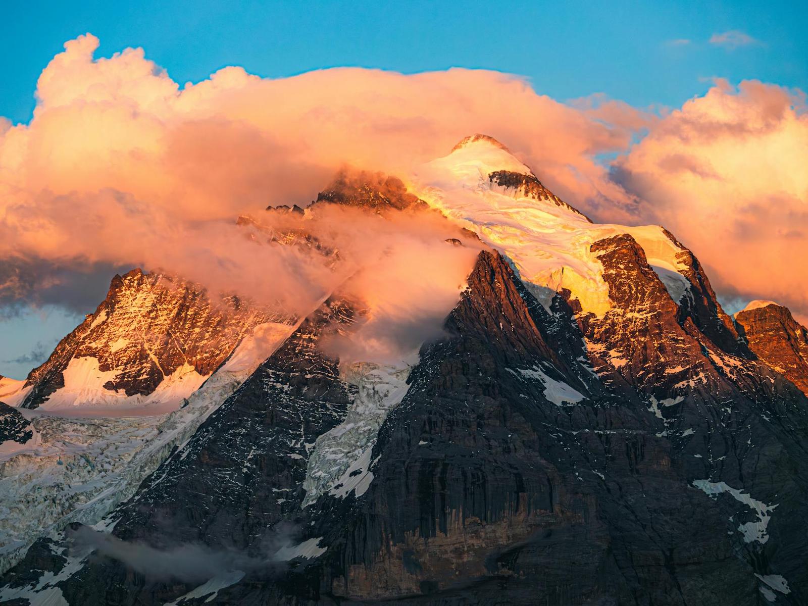 Snow and cloud wreathed mountain summit glowing at sunset