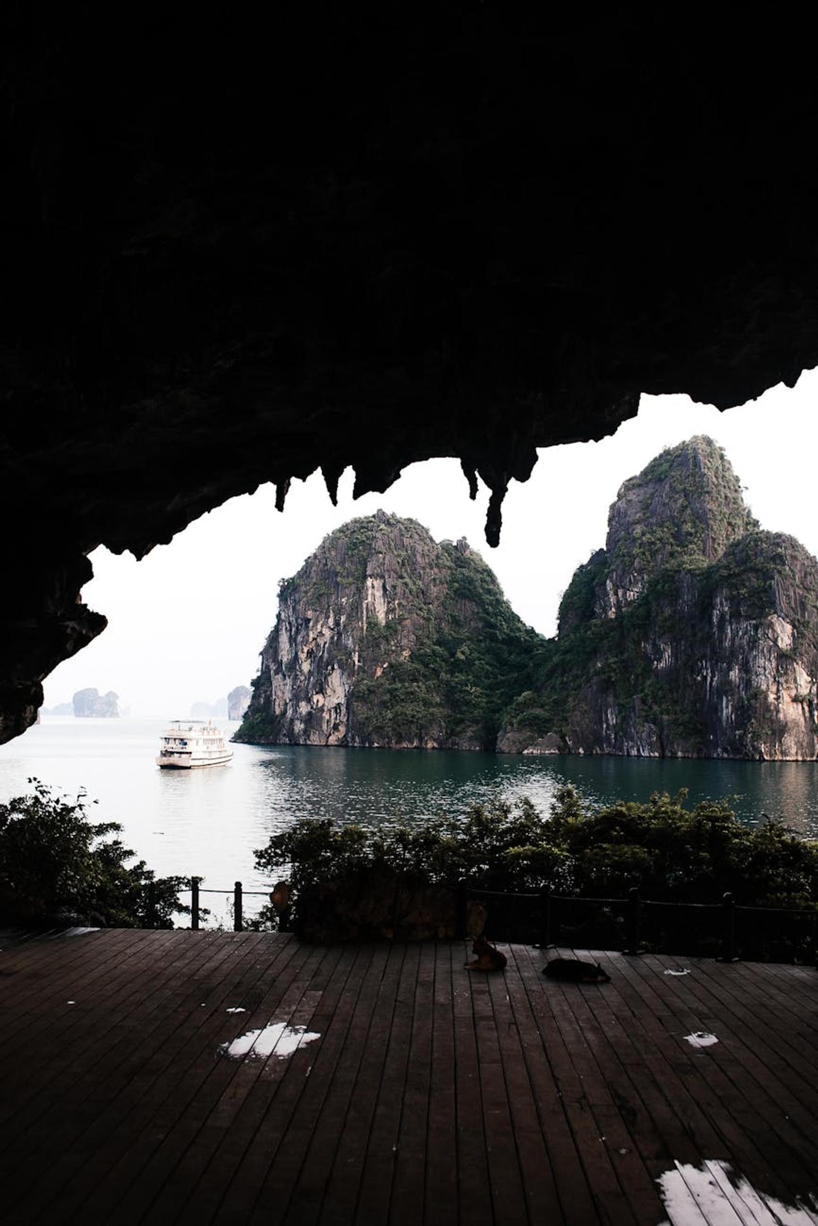 Cave opening framing limestone karsts and a cruise boat on the bay