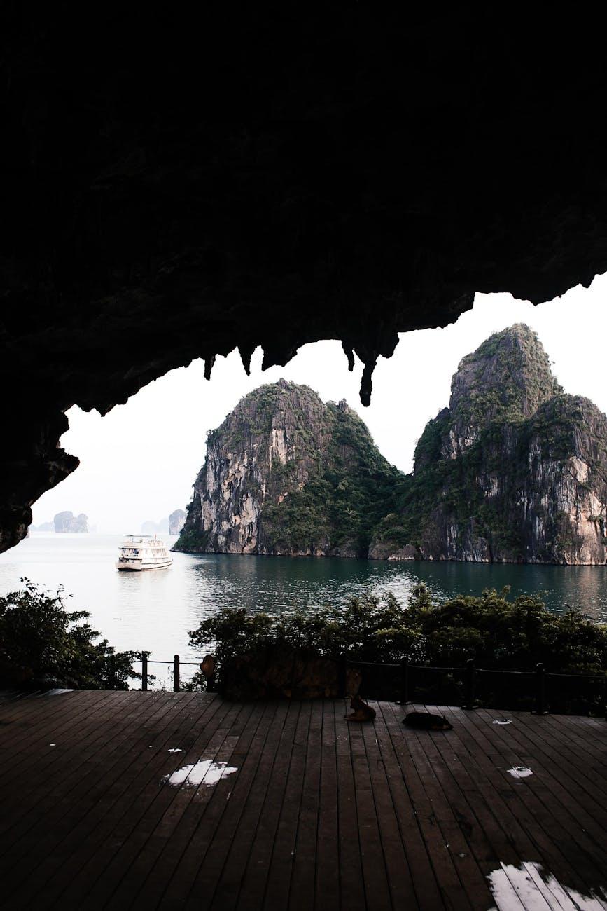 Cave opening framing limestone karsts and a cruise boat on the bay