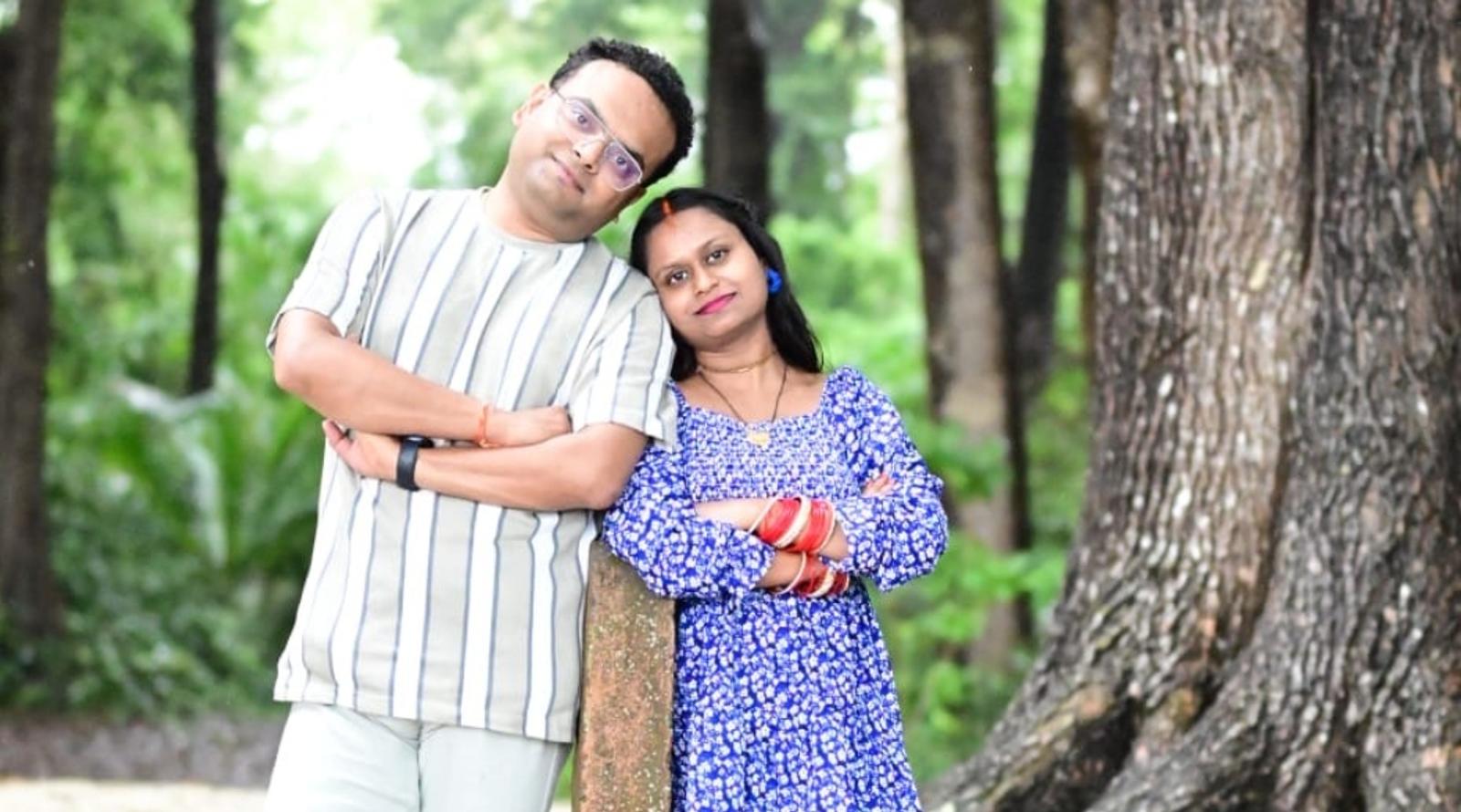 A couple posing together in a forested area, leaning on a post