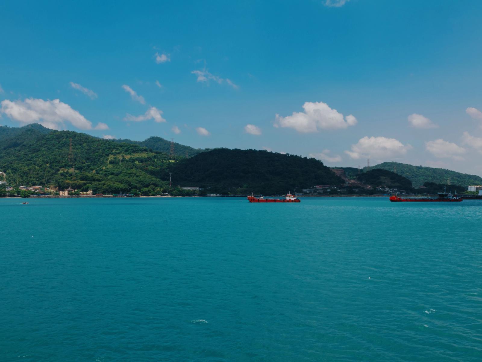 A vibrant view of cargo ships on the turquoise sea against Indonesia's lush coastline