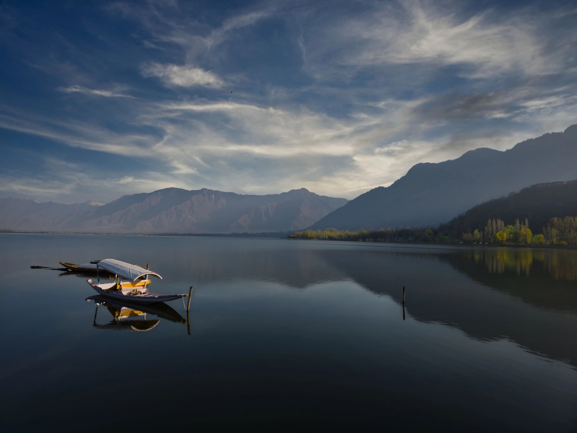 Serene boats reflect on Dal Lake with mountains in Srinagar's backdrop
