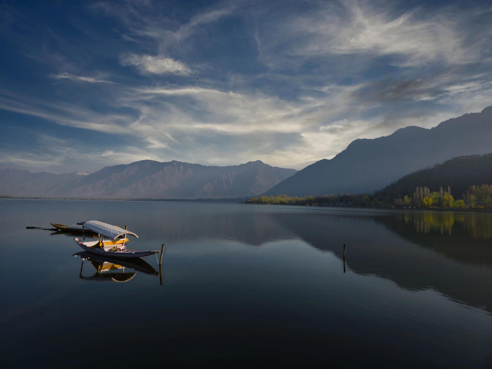 Serene boats reflect on Dal Lake with mountains in Srinagar's backdrop