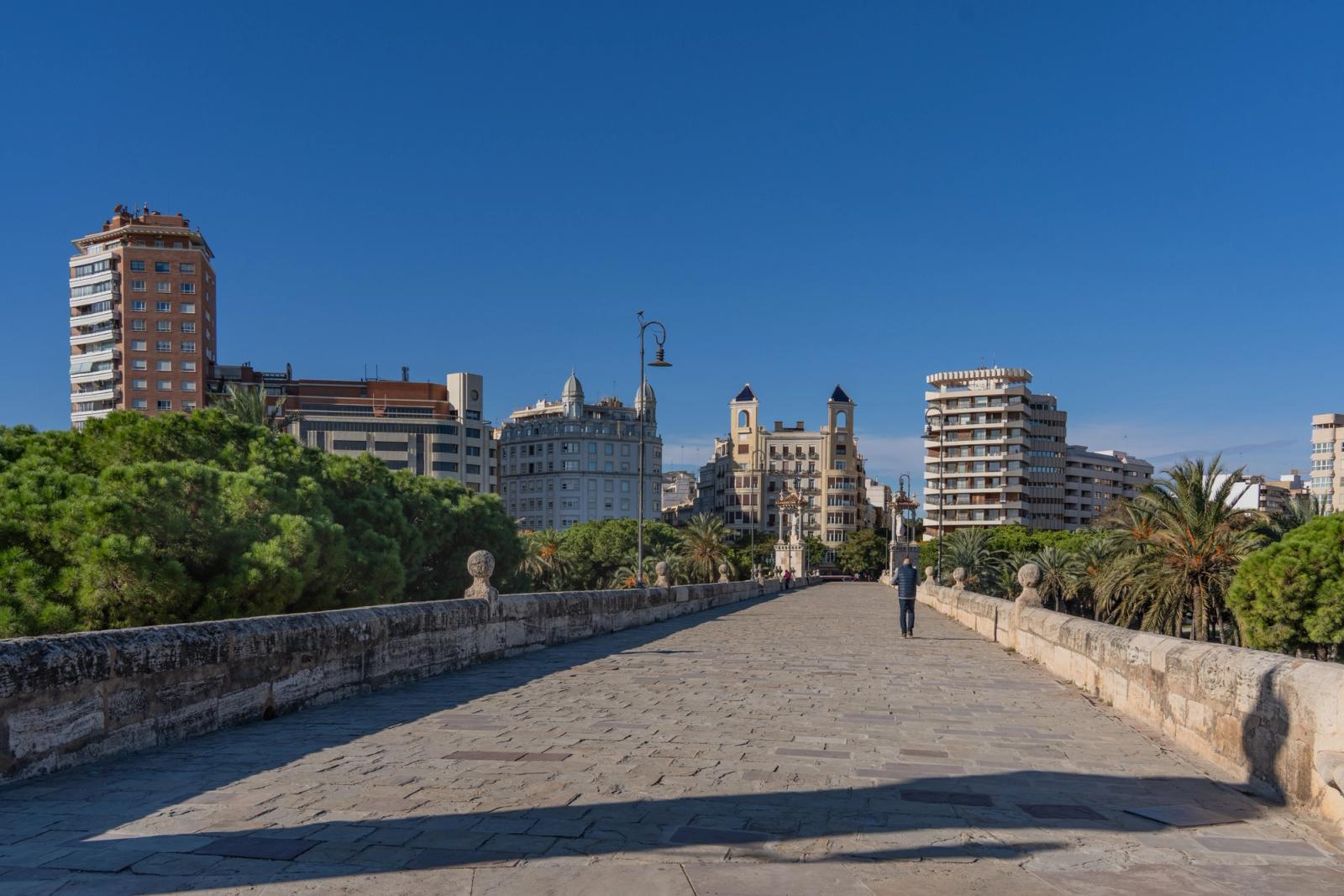 View of Valencia's skyline from a historic stone bridge on a sunny day, with clear blue skies