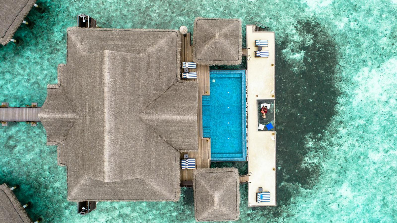 A bird's-eye view of a thatched villa roof beside a small private pool