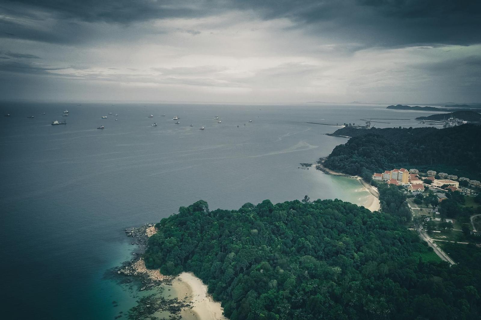 Aerial view of a forested headland and beach resort under stormy skies
