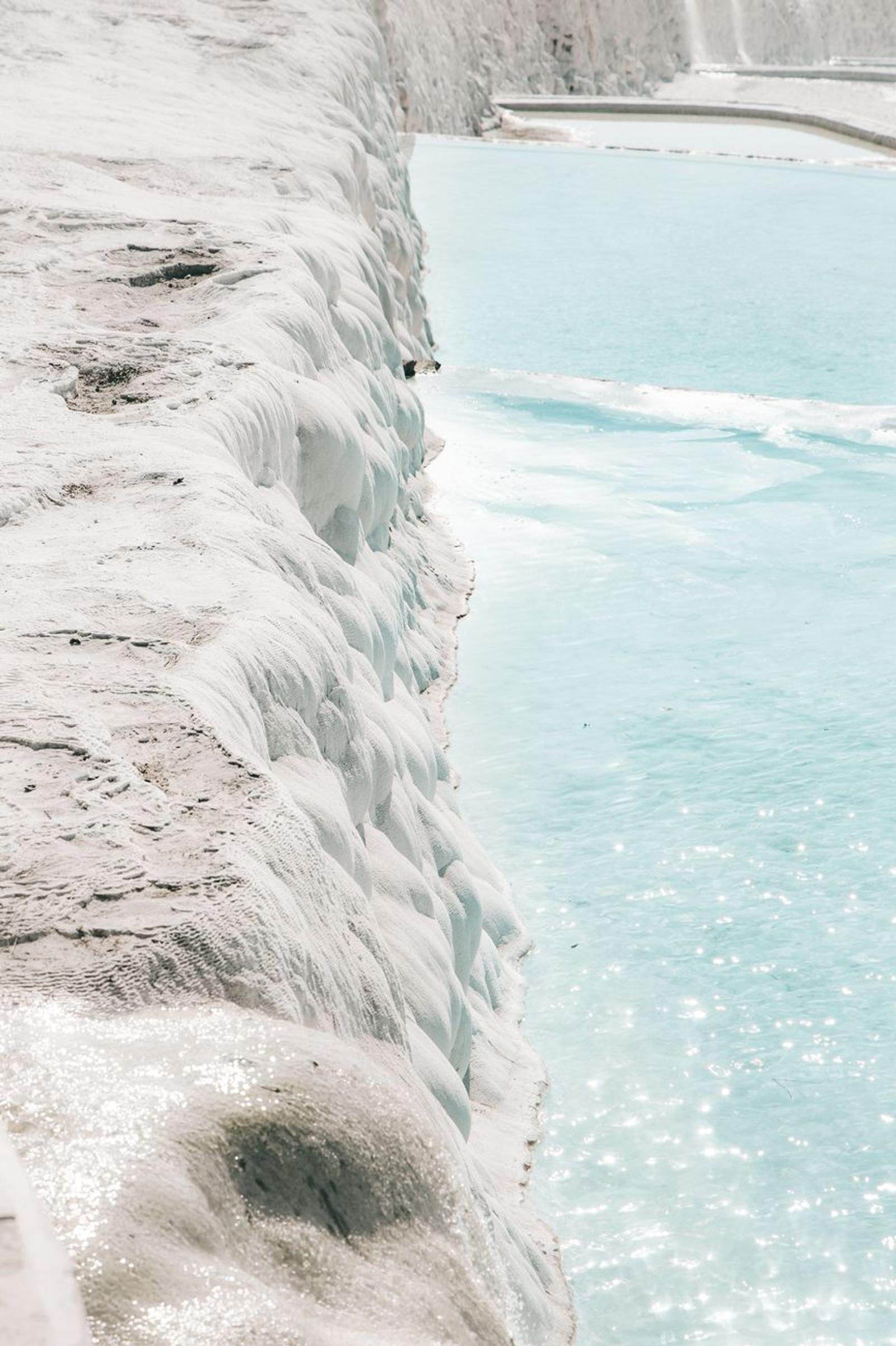 Rippled white mineral terraces beside a pale blue pool
