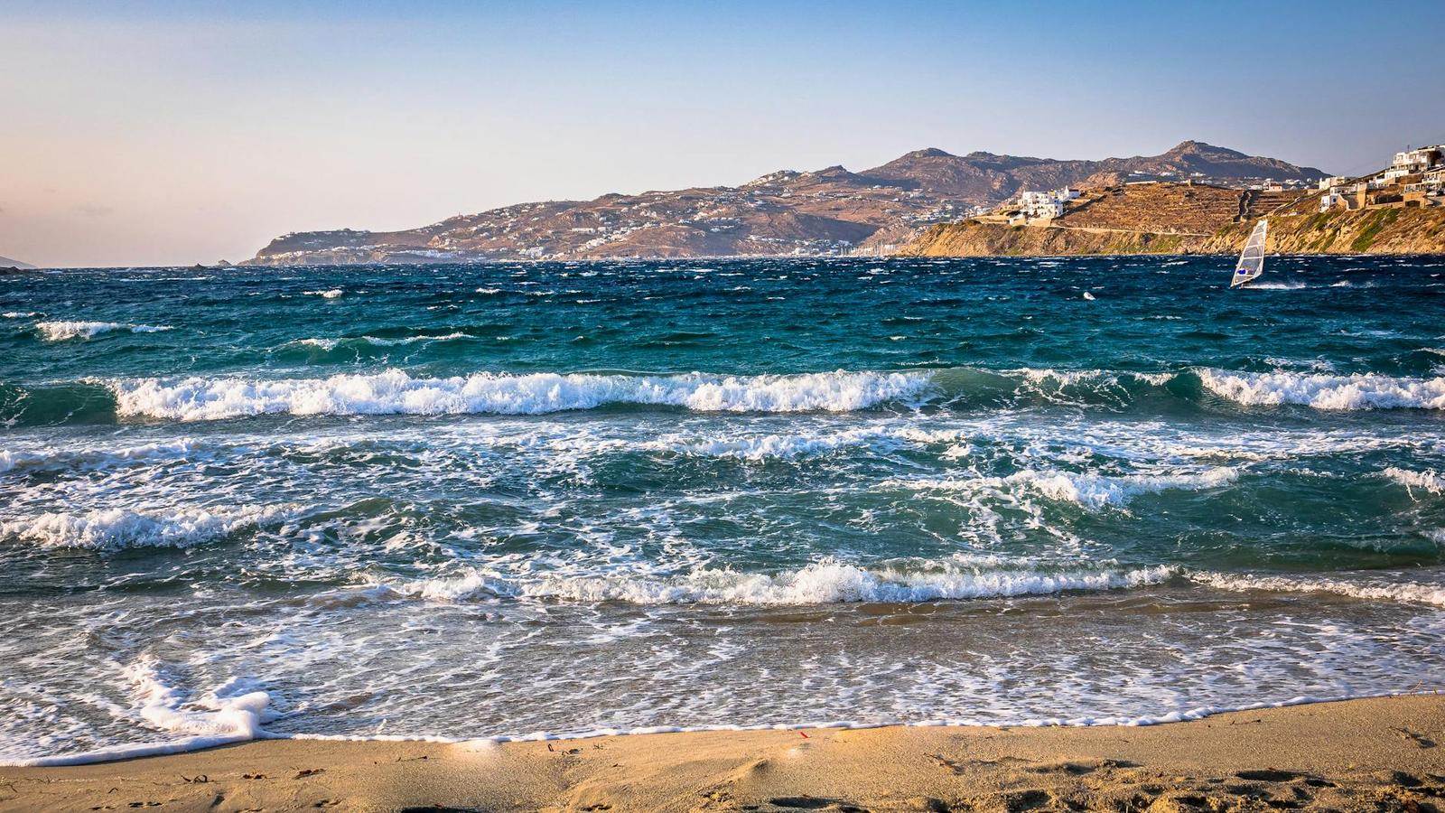 Turquoise waves rolling onto a sandy beach with hills across the bay
