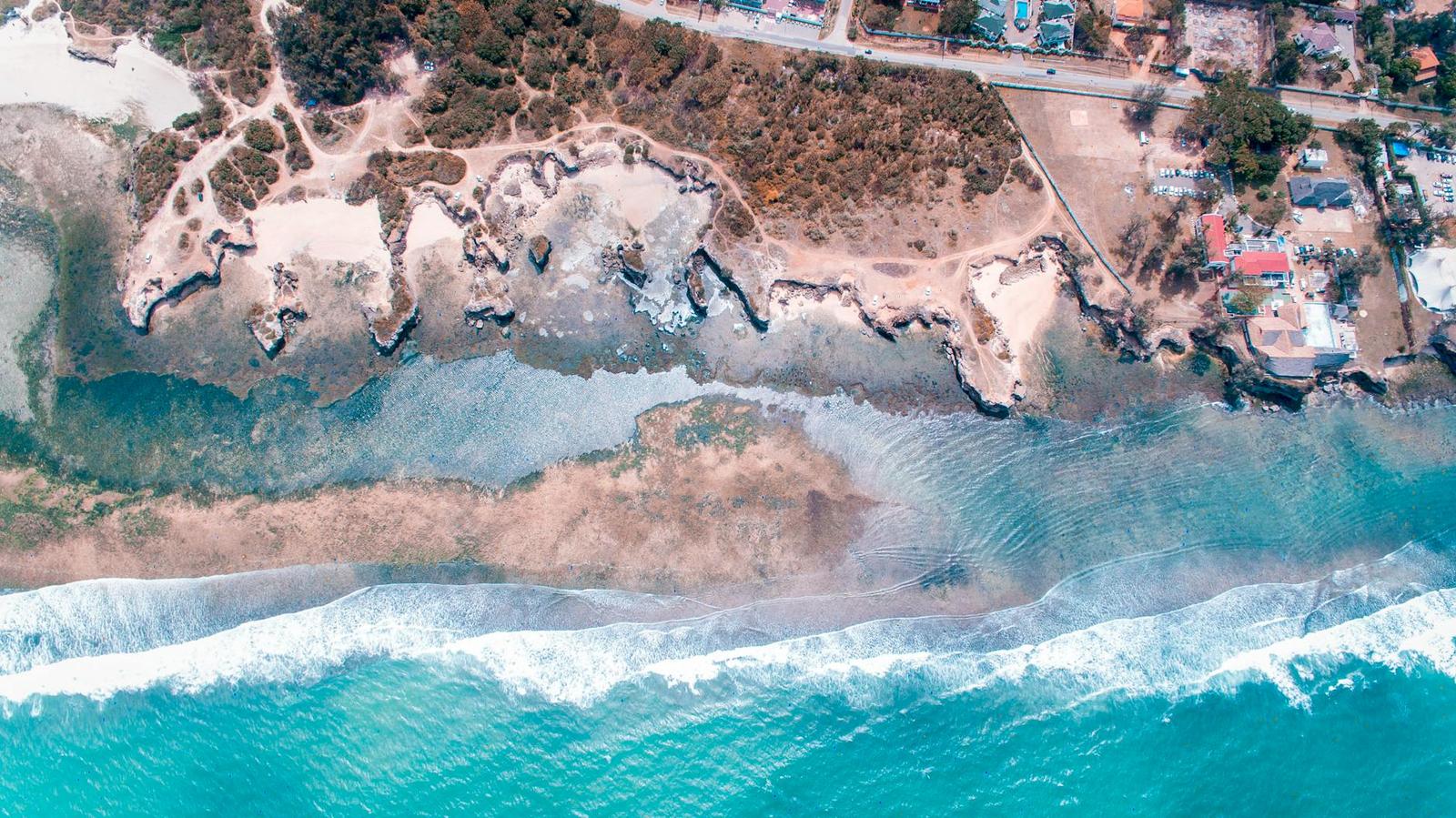 An aerial view of rocky tidal pools along a turquoise coastline