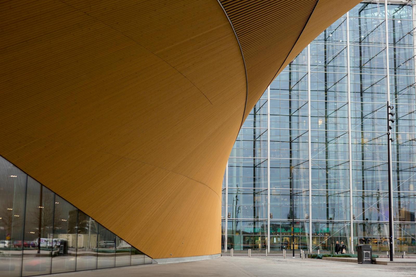 A sweeping curved wooden canopy beside a glass-fronted modern building