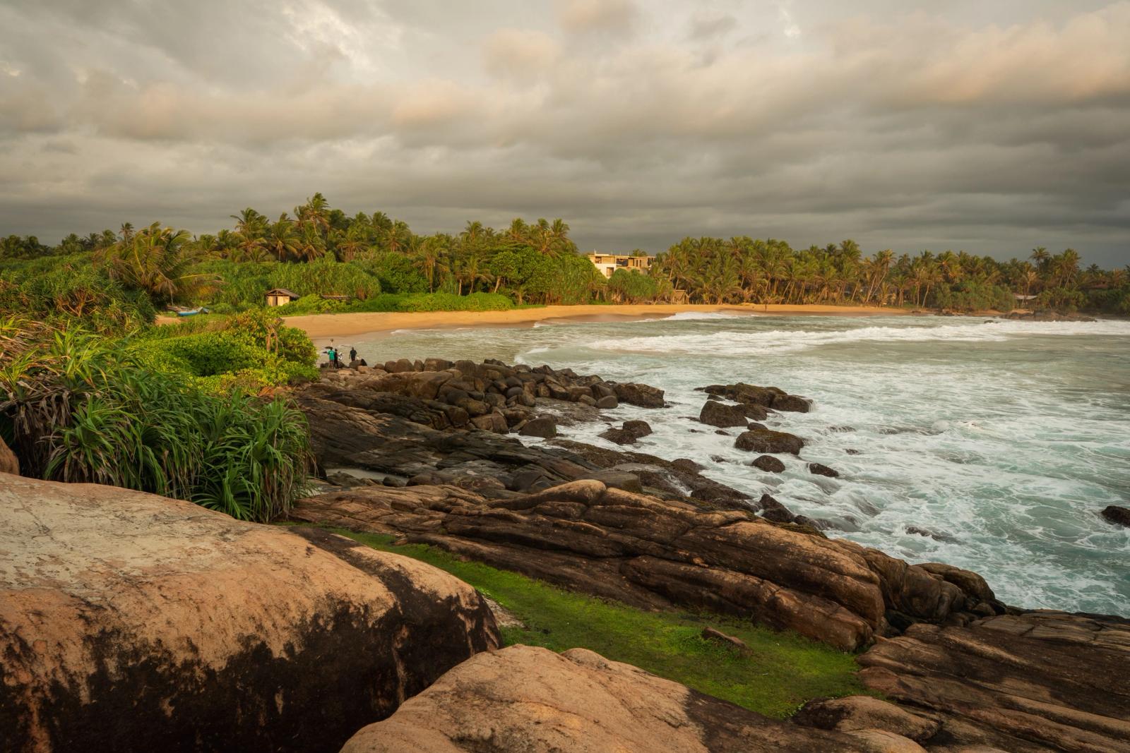 Serene tropical beach with lush greenery and rocky coastline at sunset in Sri Lanka