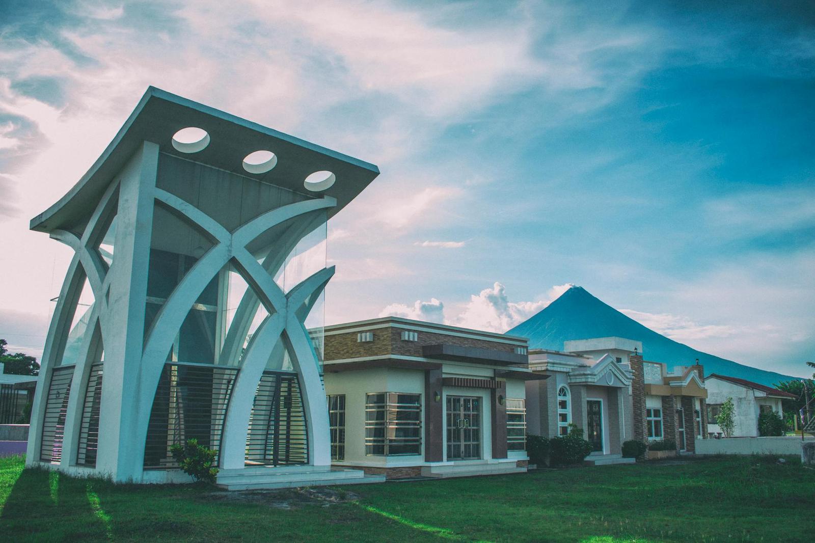 A striking modern building juxtaposed with the iconic Mayon Volcano under a bright sky