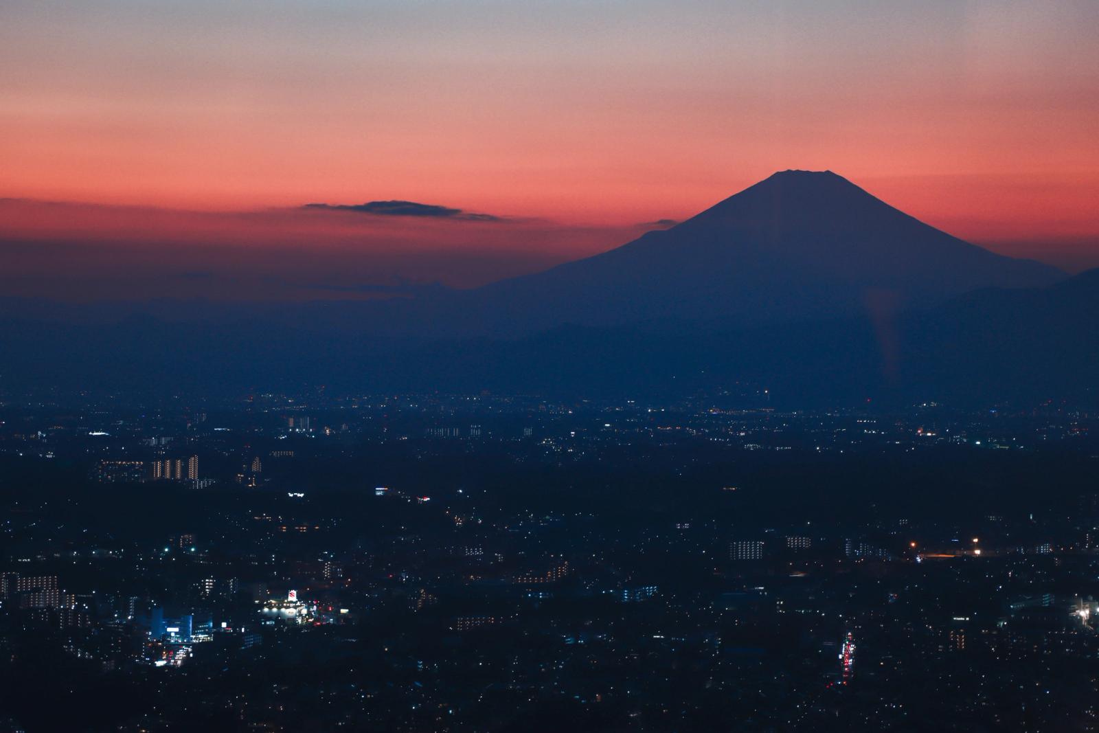 Mount Fuji silhouetted against a vibrant twilight sky over a bustling cityscape