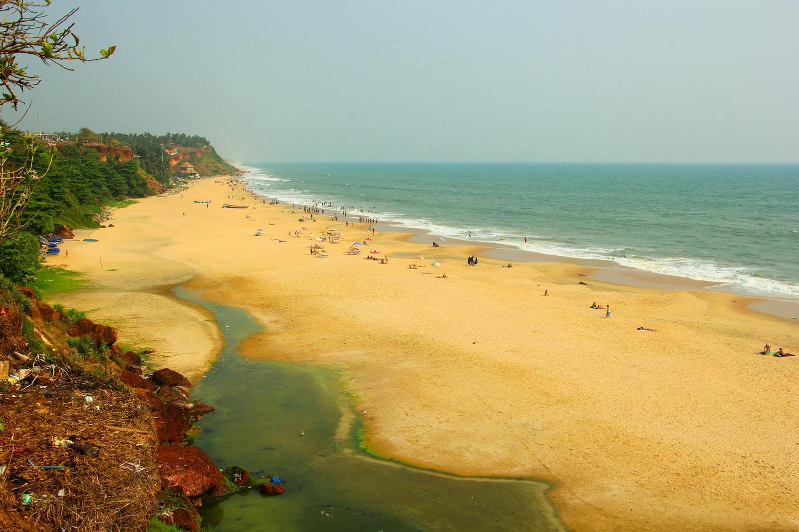 A wide golden beach curving along the coast with a small lagoon inlet