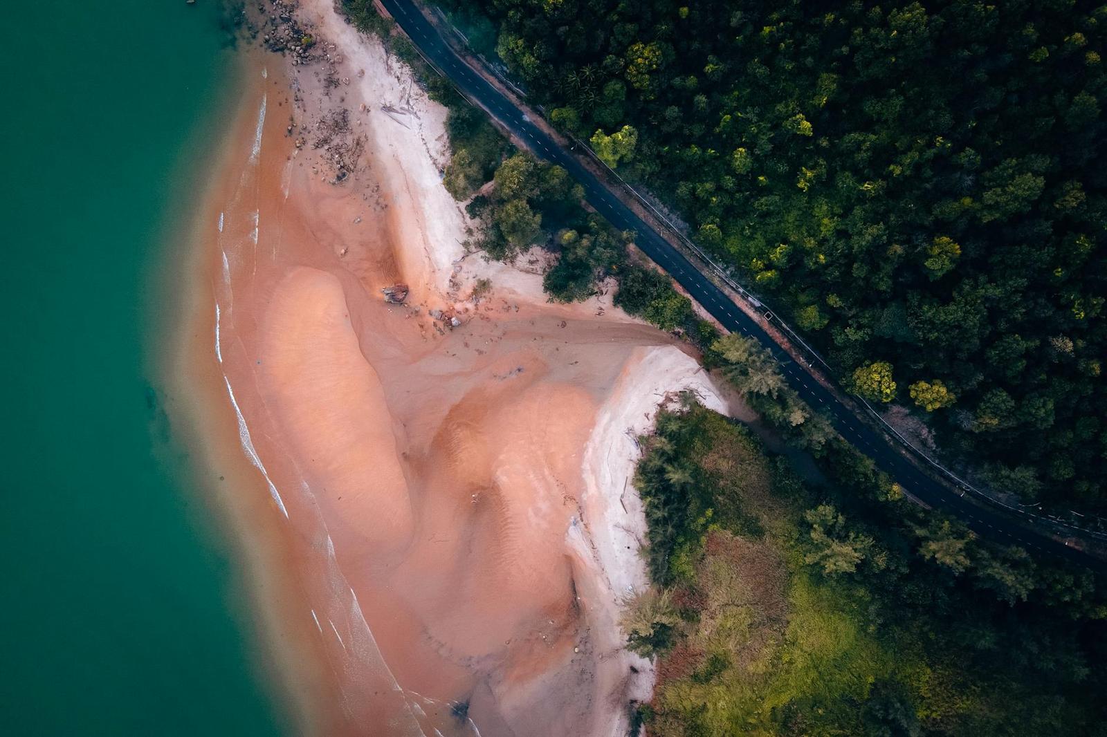 Aerial view of rust-coloured eroded cliffs meeting turquoise water beside a coastal road
