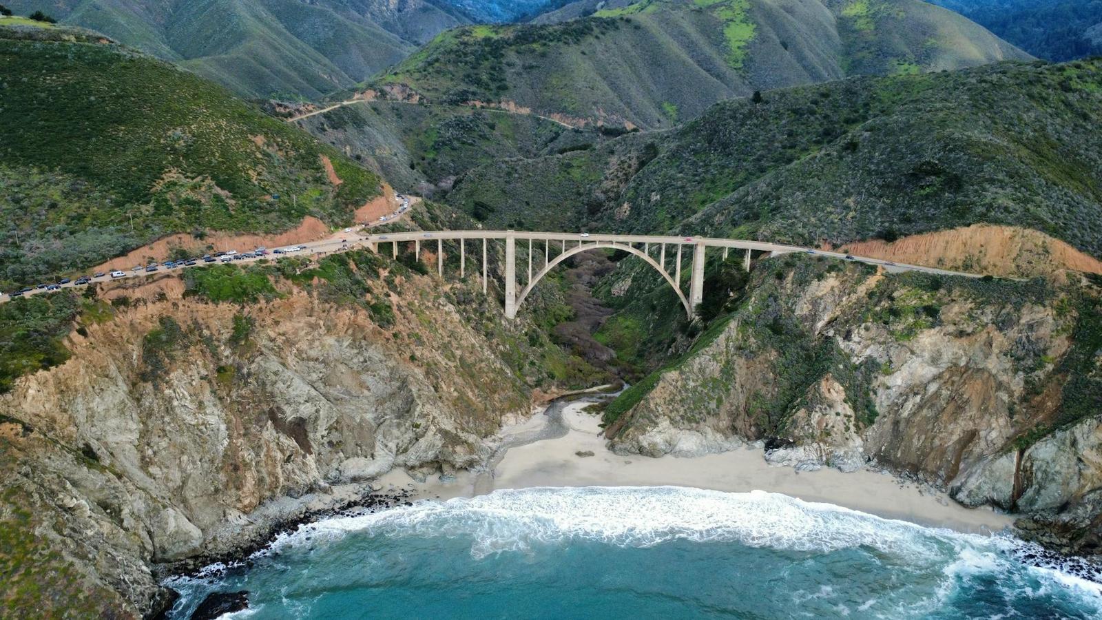 An arched bridge crossing a green canyon above a secluded beach