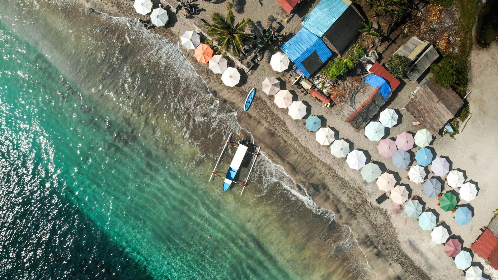 Aerial view of colourful beach umbrellas lined along the shore with a moored boat