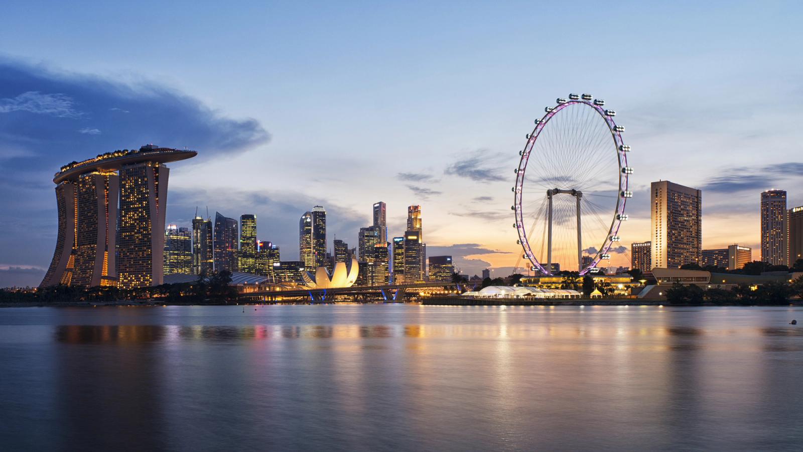 A waterfront skyline with a hotel and a large ferris wheel at dusk