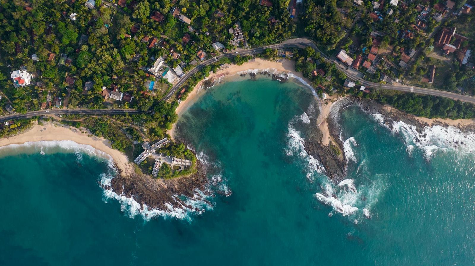 Aerial view of a wooded headland separating two turquoise coves