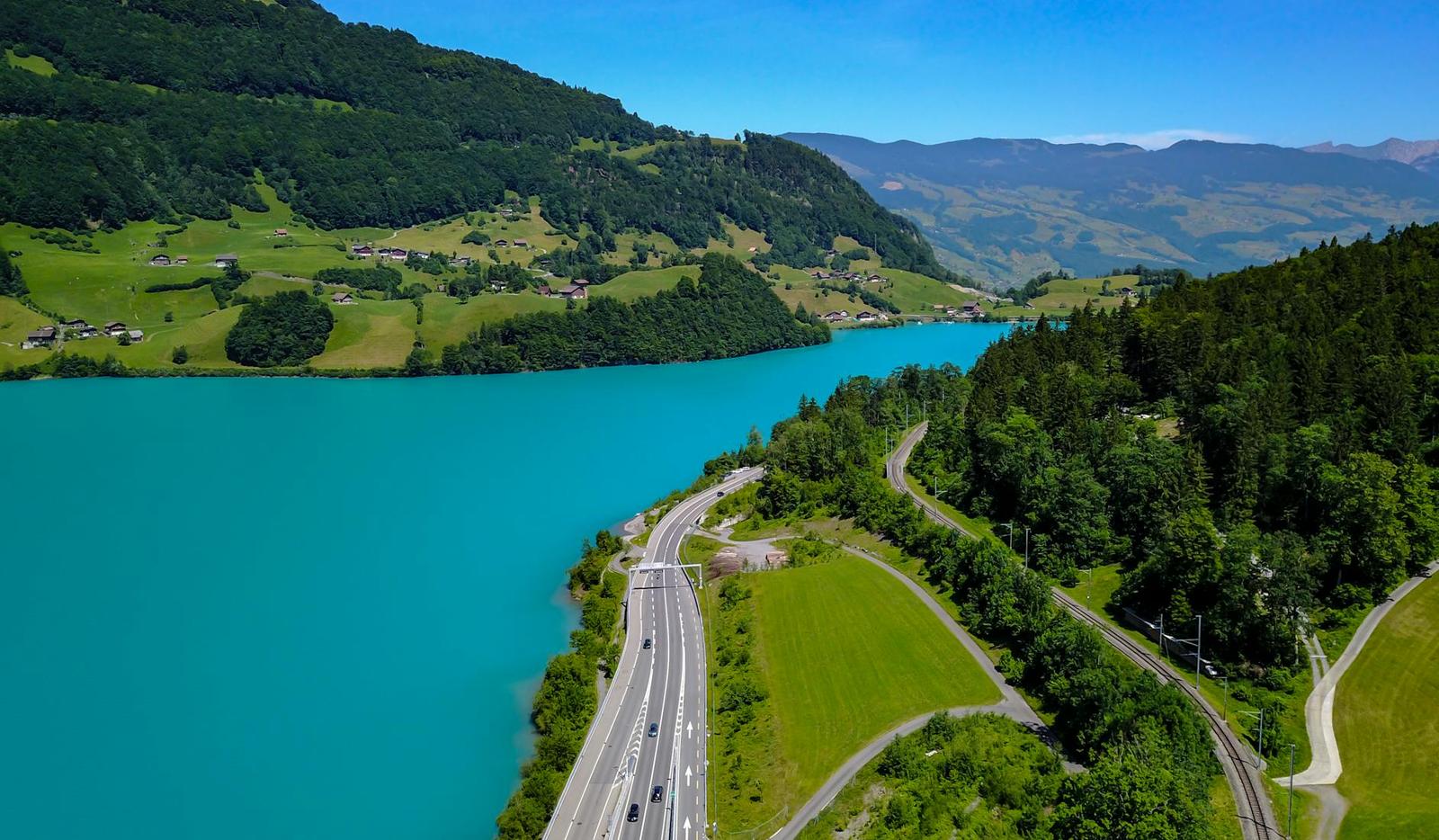 Aerial view of a turquoise reservoir with a road curving along green hillsides