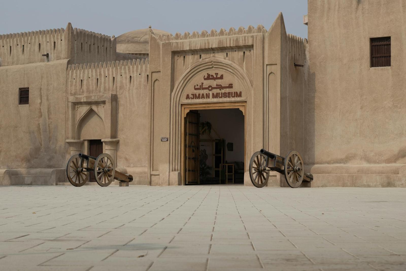 A sand-colored fort building with an arched doorway and two old cannons in the courtyard