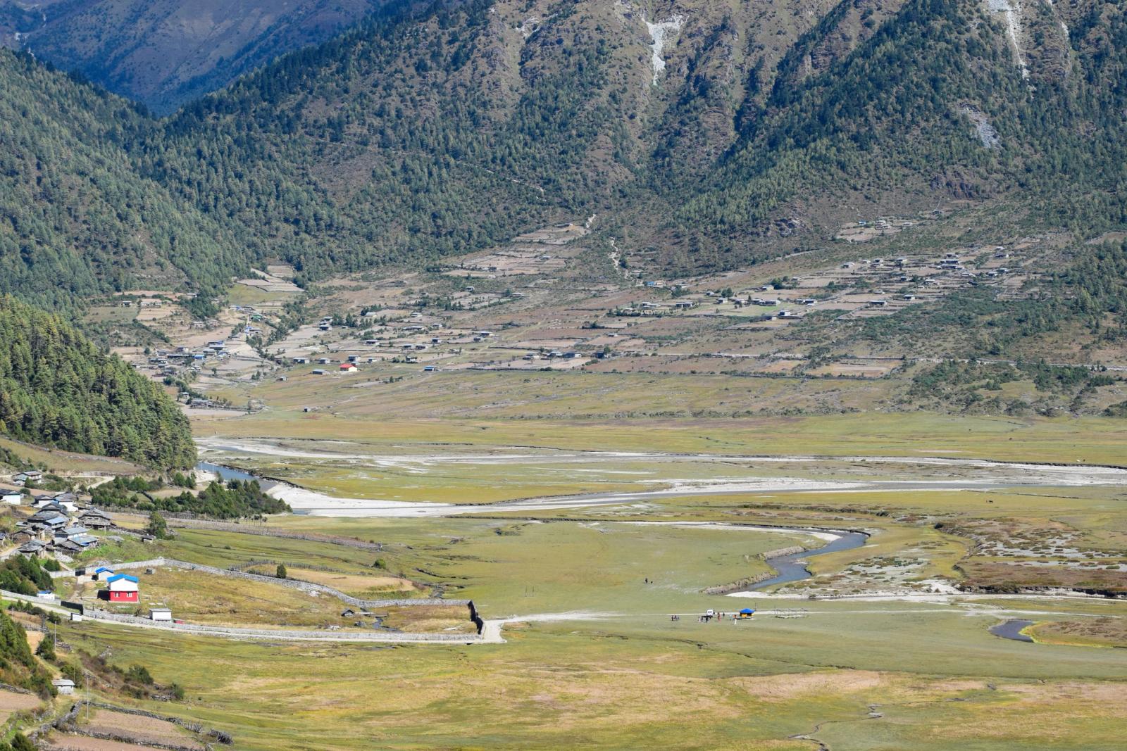 Expansive mountain valley with lush greenery and rural settlements captured during daytime in early autumn