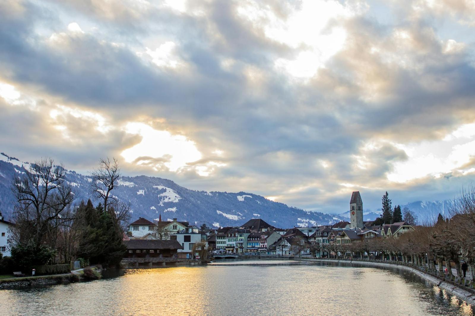 Riverside village with a church spire framed by snow-capped mountains at dusk