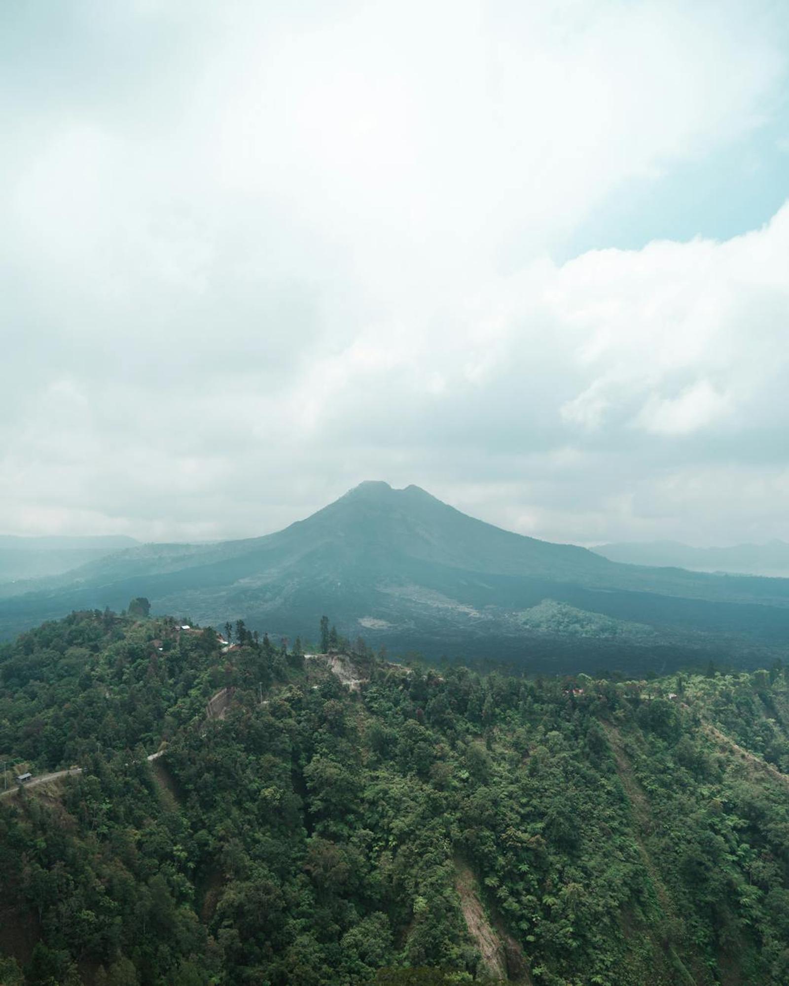 Stunning landscape view of Mount Batur surrounded by lush forests under a cloudy sky in Kintamani, Bali
