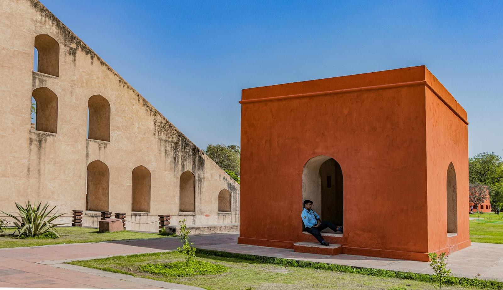 Person resting in an orange arched alcove beside ancient stone instruments