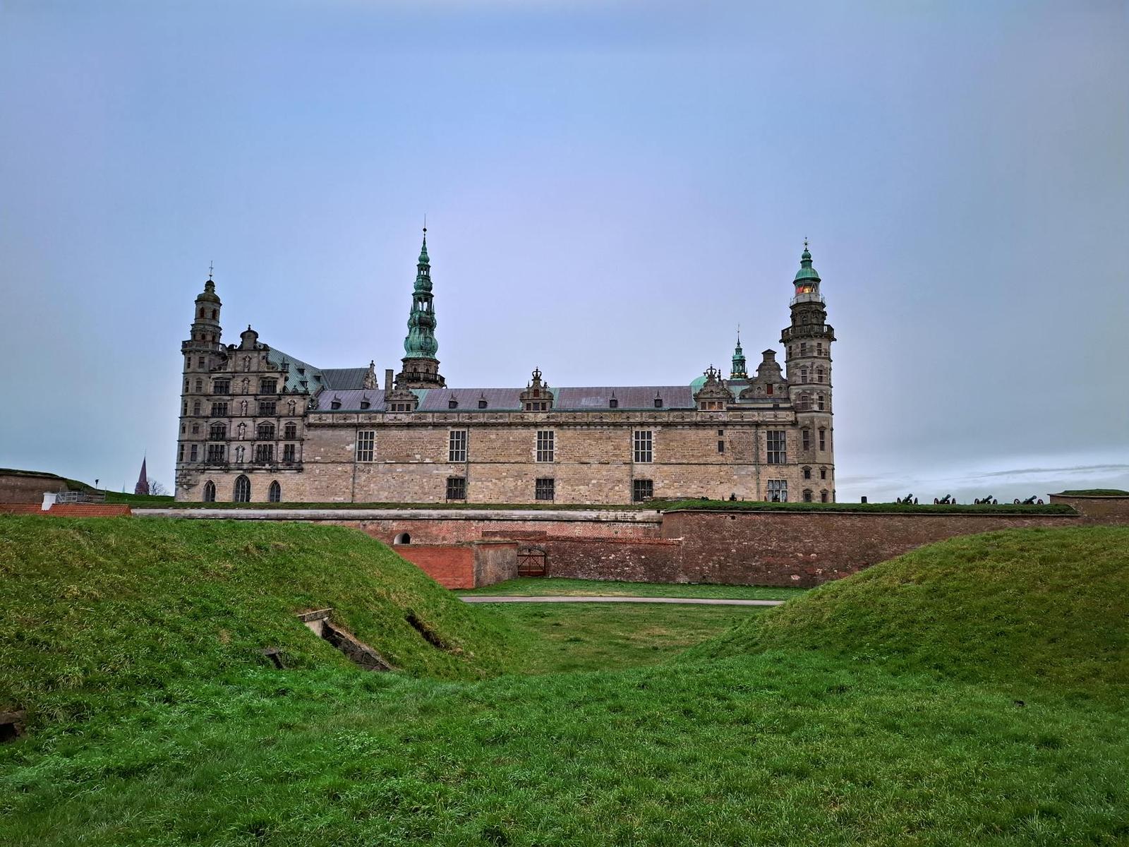 A long stone castle with spired towers seen across a grassy moat