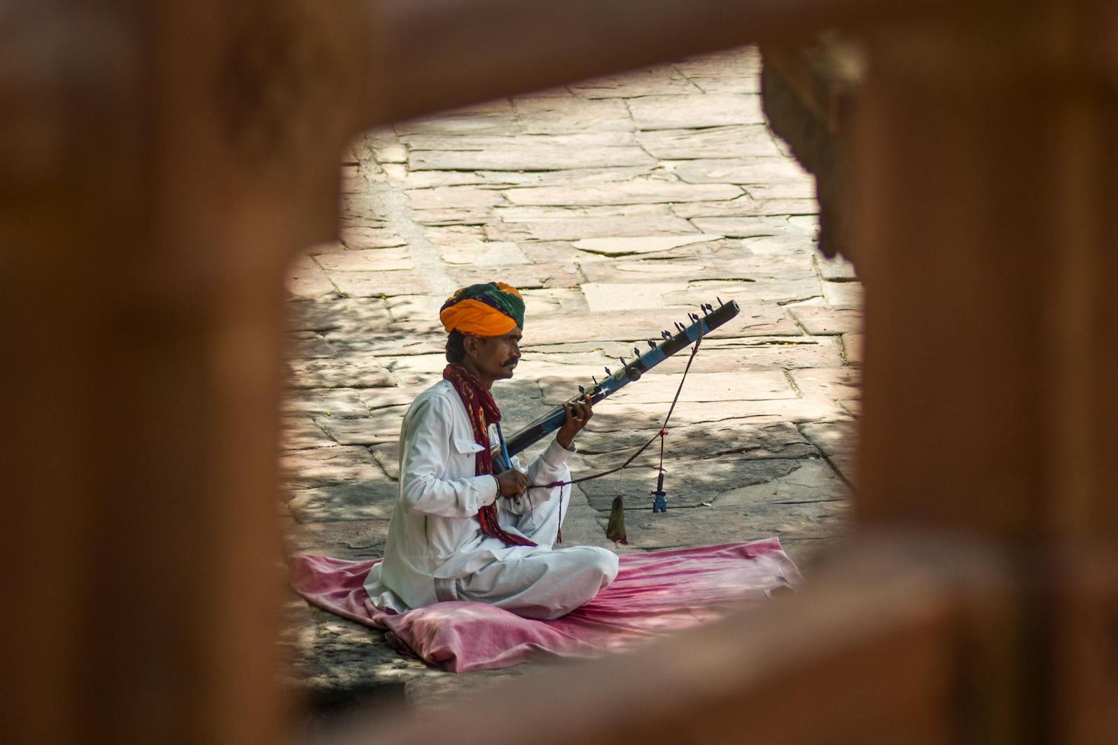A musician playing a stringed instrument seated on a pink cloth