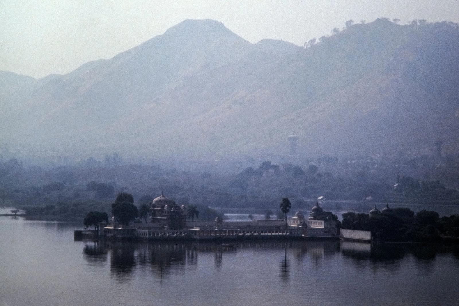A serene landscape showcasing a lake and hills in Udaipur, India, enveloped in mist and tranquility