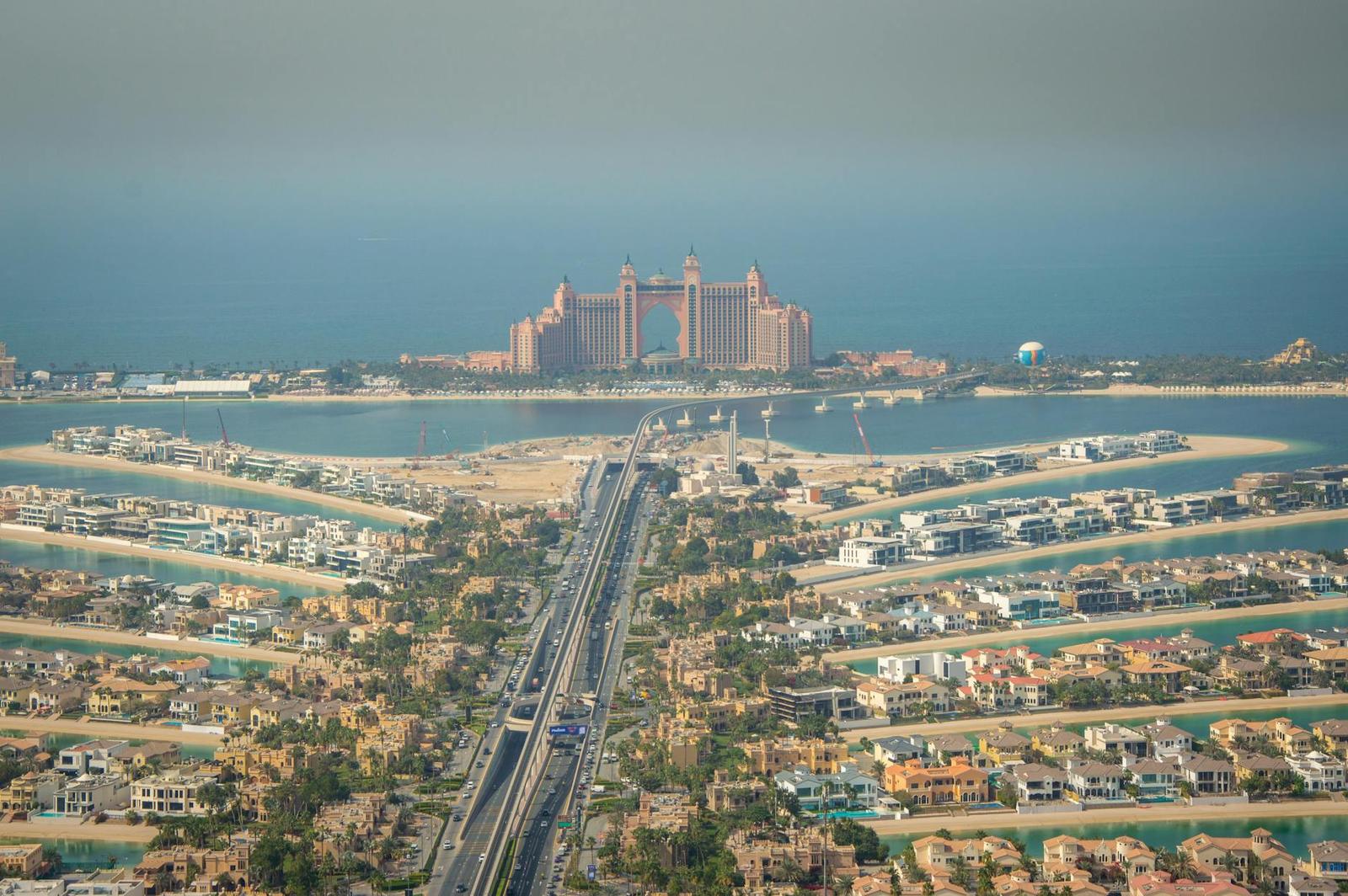 An aerial view of a palm-shaped man-made island with a grand pink resort at its tip