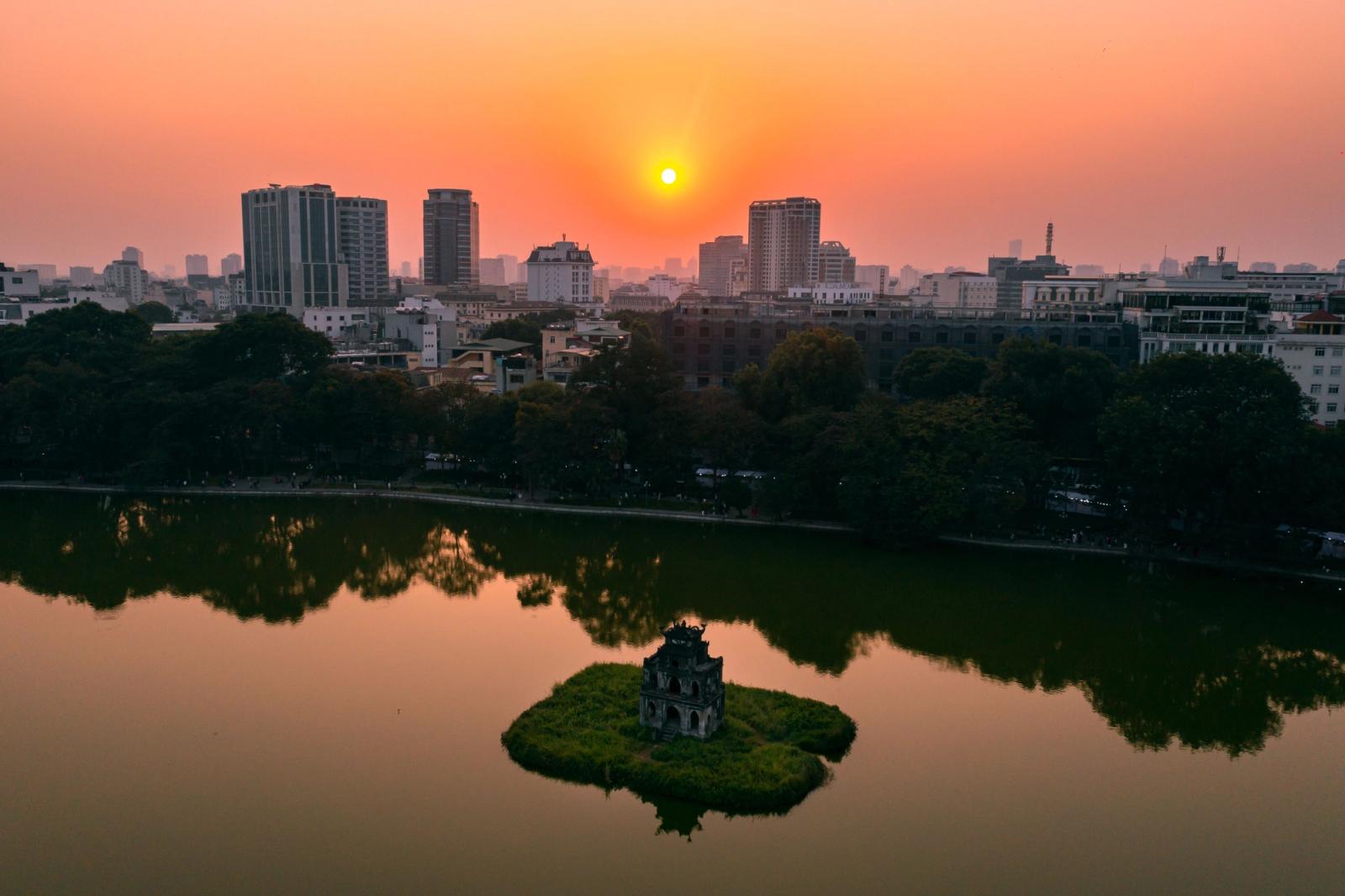A beautiful sunset over Hanoi's skyline, featuring the iconic Hoan Kiem Lake and Turtle Tower reflections