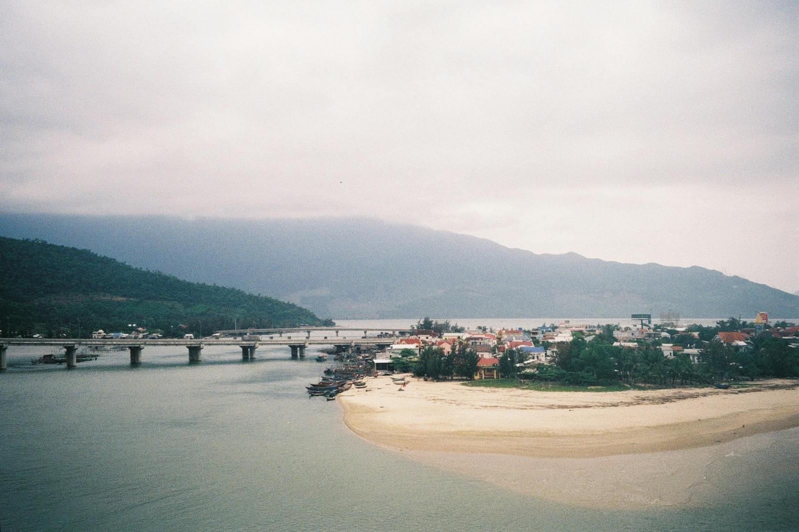 Long bridge spanning a river mouth beside a sandy spit and misty hills