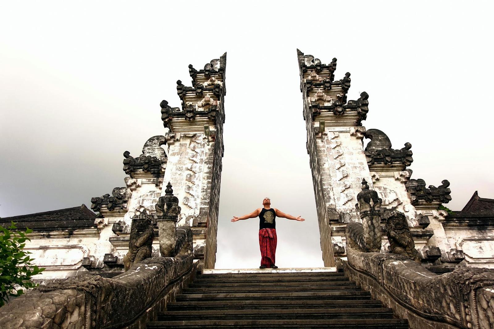 A figure stands with arms outstretched between towering carved stone temple gates