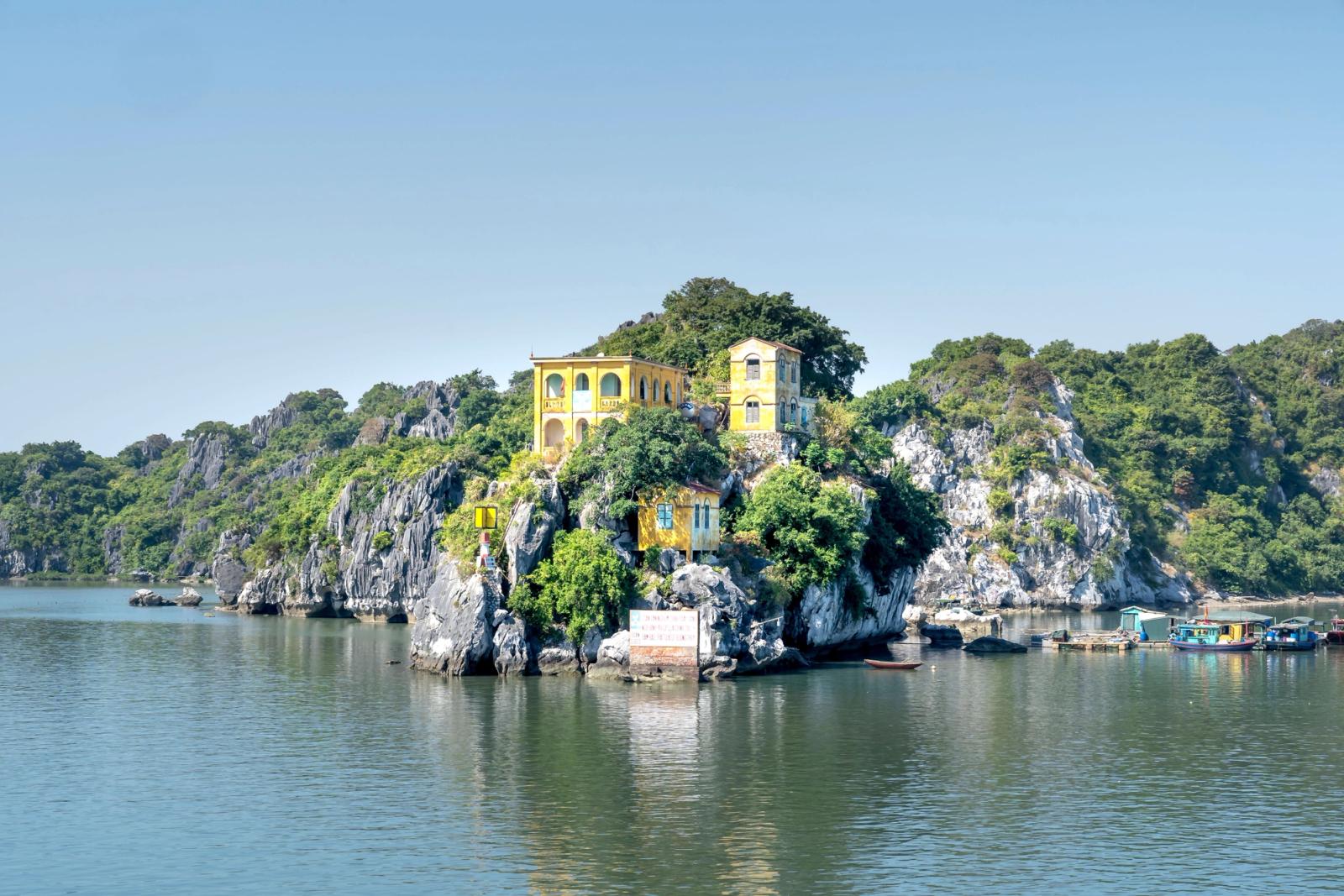 Scenic view of a vibrant yellow house perched on lush cliffs in Halong Bay, Vietnam
