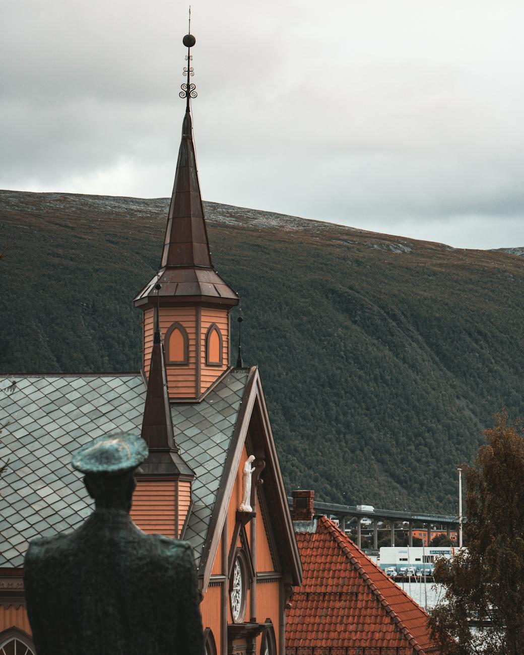Scenic view of a Gothic church tower in Tromsø, with mountainous backdrop