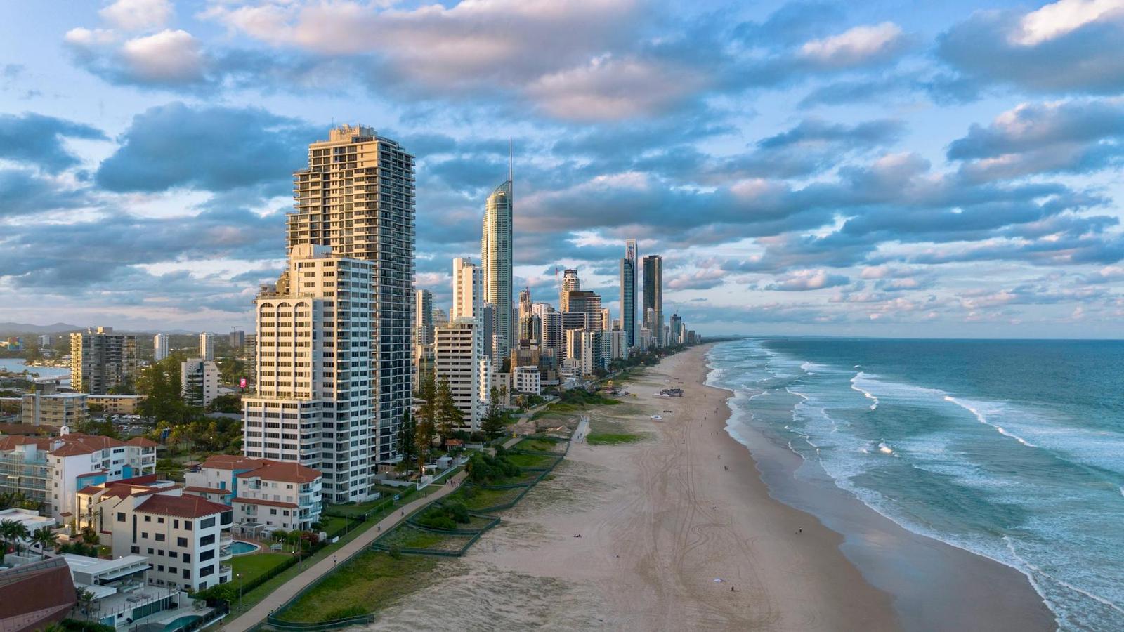 A curved shoreline of high-rise apartments meeting a wide sandy beach at sunset