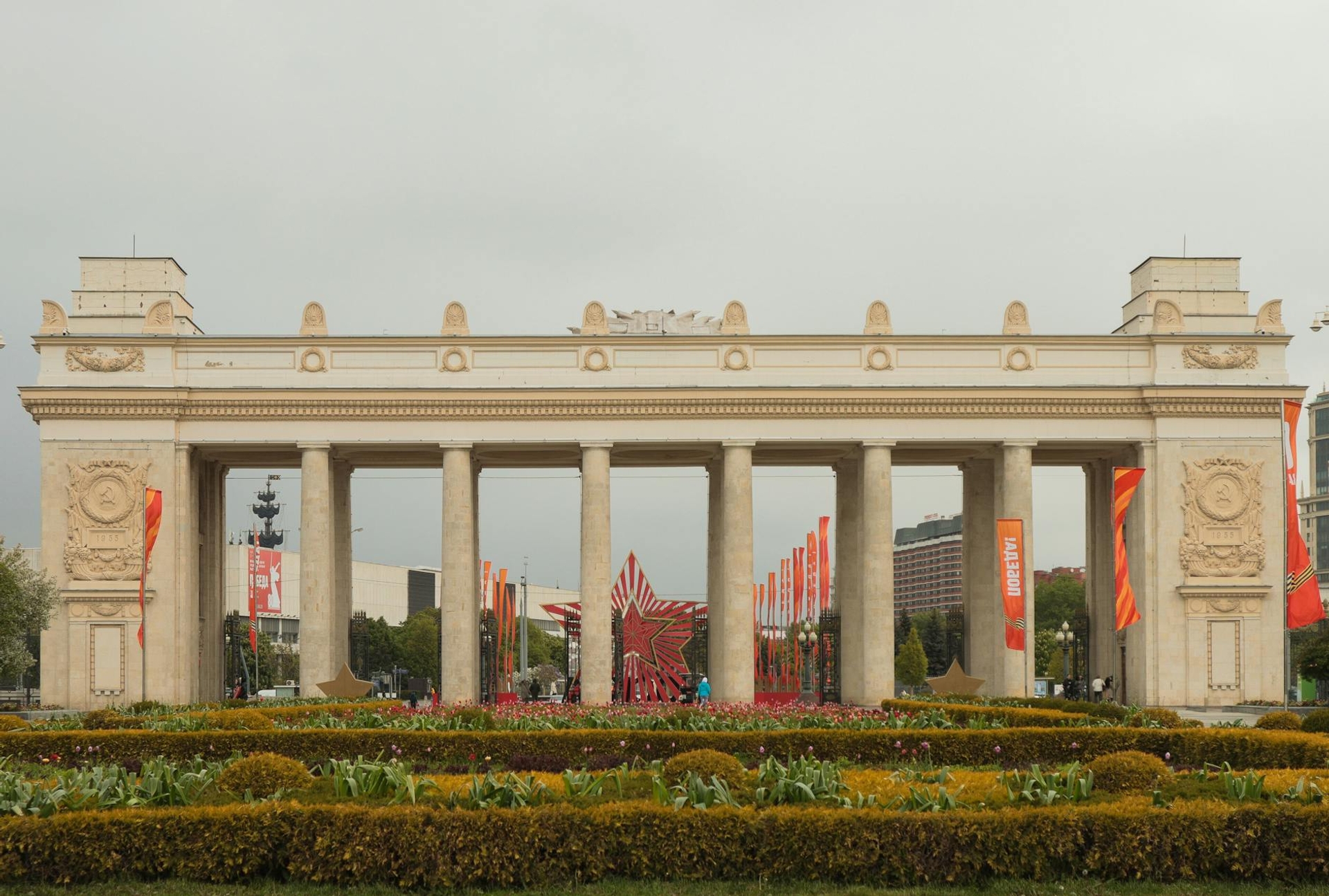 A neoclassical colonnaded gateway framed by flowerbeds in a city park