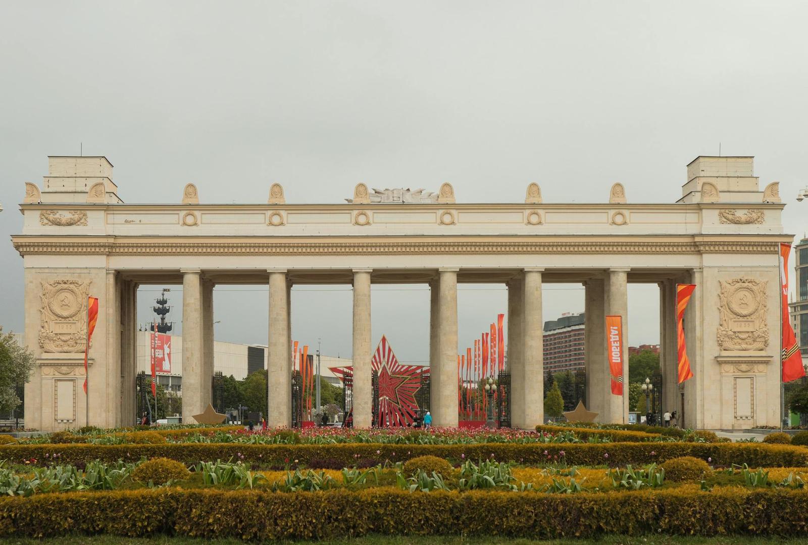 A neoclassical colonnaded gateway framed by flowerbeds in a city park